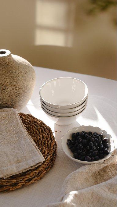 a table with a bowl of blueberries and a plate of white dishes